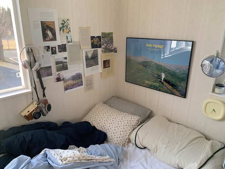 白い壁とヴィンテージ小物が配された居心地の良い一人寝室、枕とポスターがあるコンパクトな空間