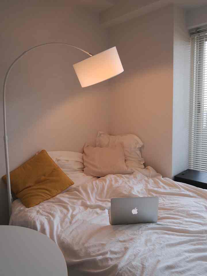 ライトグレーのトーンの小さな寝室、白いベッドと枕、フロアランプが配置された居心地の良いインテリア