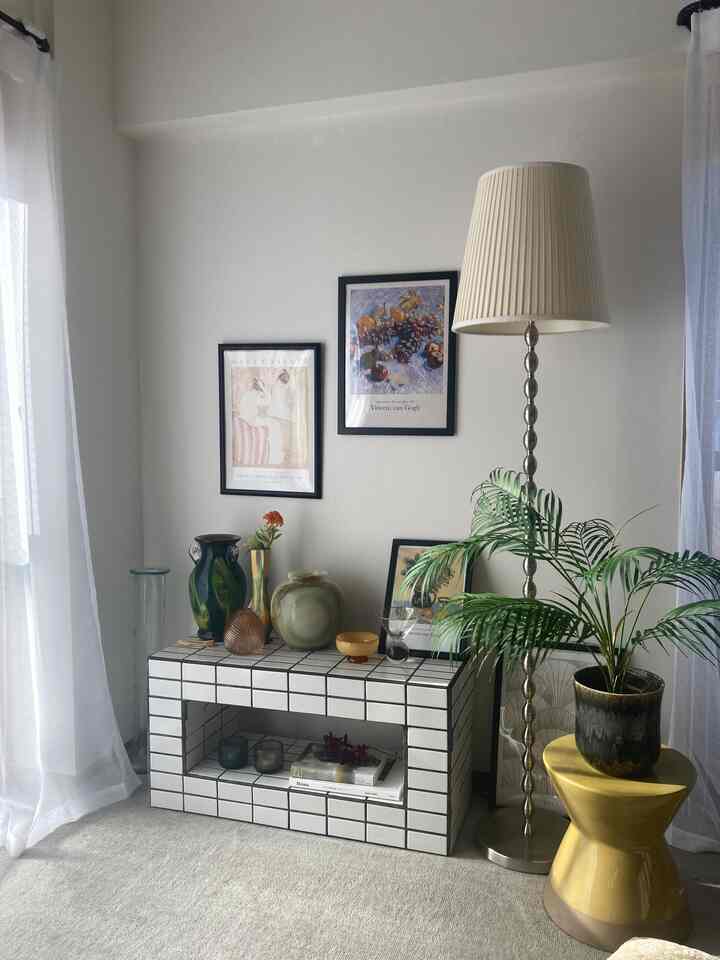 白い壁とタイルのコンソールテーブルがあるナチュラルでシンプルなリビング、ポスターと大きな観葉植物、フロアランプが配置された印象的な空間