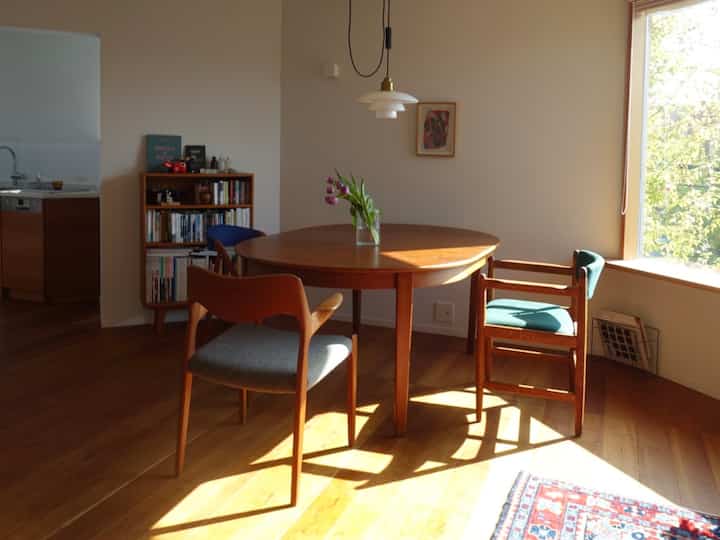 暖かい木目調の床と円形のダイニングテーブルに花瓶が置かれたナチュラルなダイニング空間