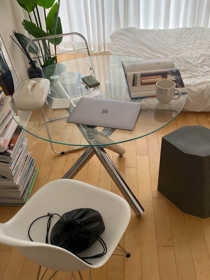 ナチュラルな床と透明なガラステーブルがあるワンルームのリビング、コンパクトでシンプルなホームオフィス空間