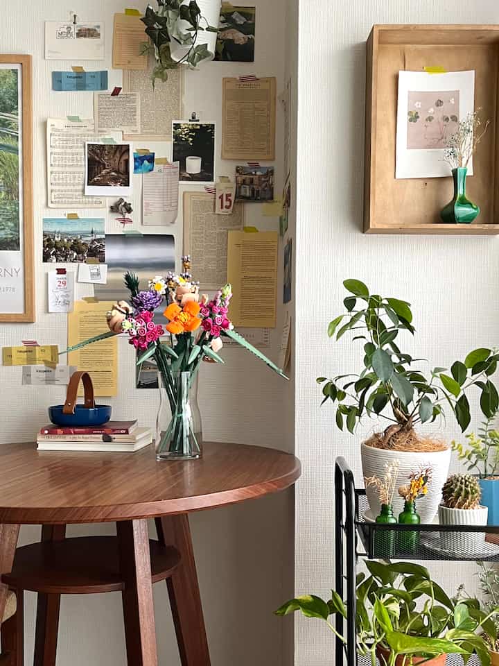 ナチュラルなブラウンウッドのダイニングテーブルにカラフルなLEGOの花束、壁には色々な紙が飾られ、植物が配置された雰囲気のあるキッチンインテリア