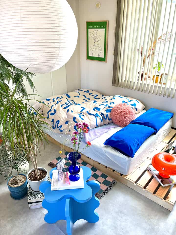 白と青のトーンの寝室、ナチュラルな木製ベッドとサイドテーブル、植物が配置された明るくモダンなインテリア