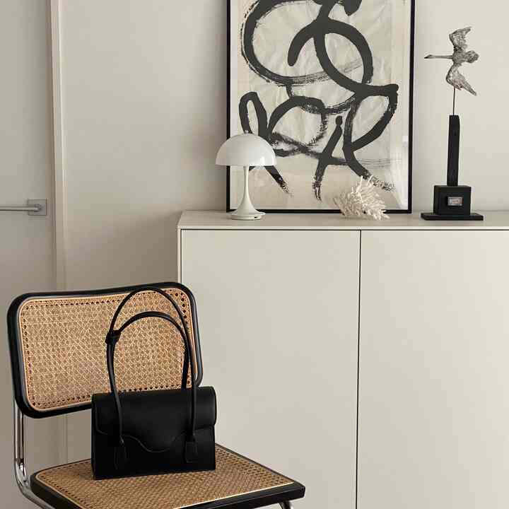 ナチュラルカラーの玄関スペース、ラタンのアームチェアに黒いバッグとシンプルなキャビネットの上に白いテーブルランプが配置された雰囲気のあるインテリア