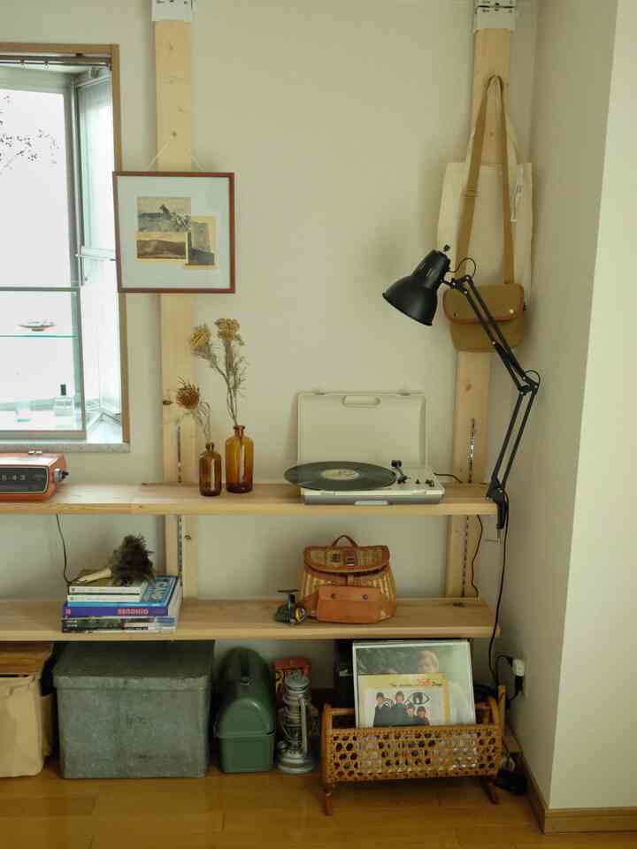 ライトグレーの壁と木目調の棚があるホームオフィス空間、ヴィンテージの音楽プレーヤーと小さな額縁が配置されたナチュラルモダンなインテリア