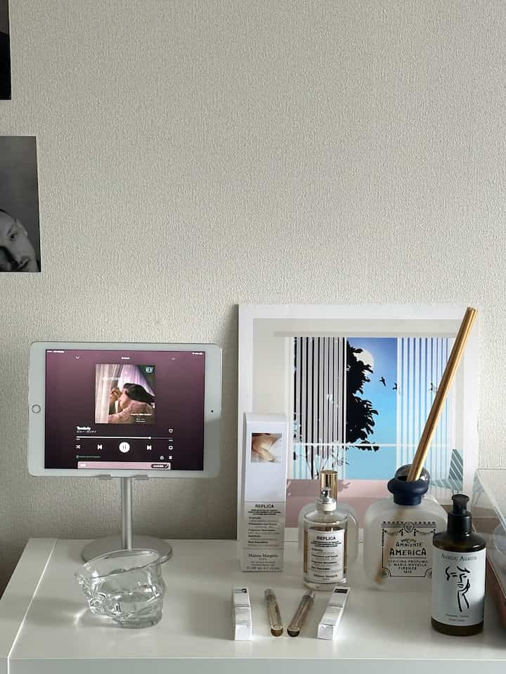 ナチュラルトーンのデスクにタブレットスタンド、香水、ディフューザーが整然と配置された雰囲気のあるホームオフィス