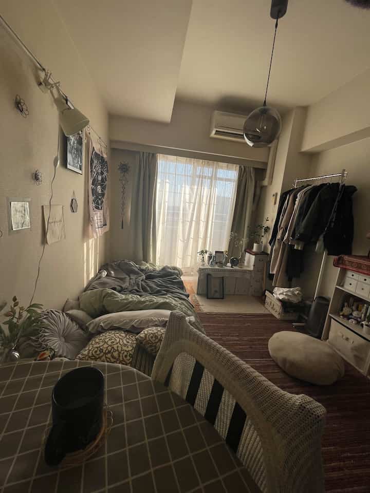 ベージュとブラウンの色調のリビング兼寝室、カーテンとラグが配置された雰囲気のあるインテリア