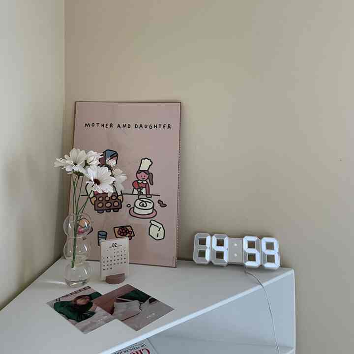 Beige-toned wall with a white shelf holding a flower vase and digital clock in a simple bedroom space