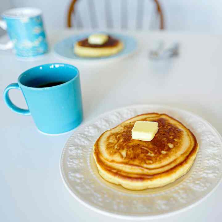 白いテーブルの上にバターがのったパンケーキと青いマグカップが置かれた北欧スタイルのおうちカフェスペース