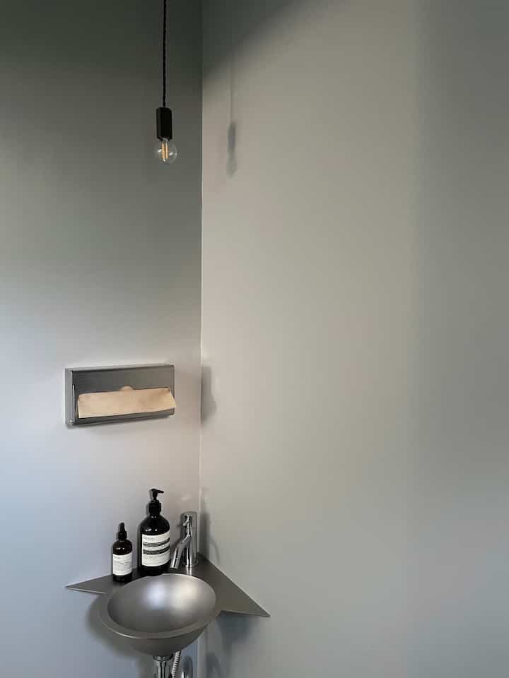 A simple and modern trendy restroom with gray walls and a stainless steel corner sink