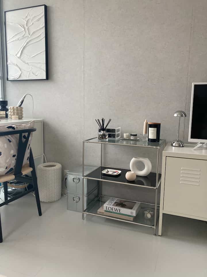Modern space in white and silver tones featuring a metal rack, cream cabinet, and wall art in harmonious arrangement