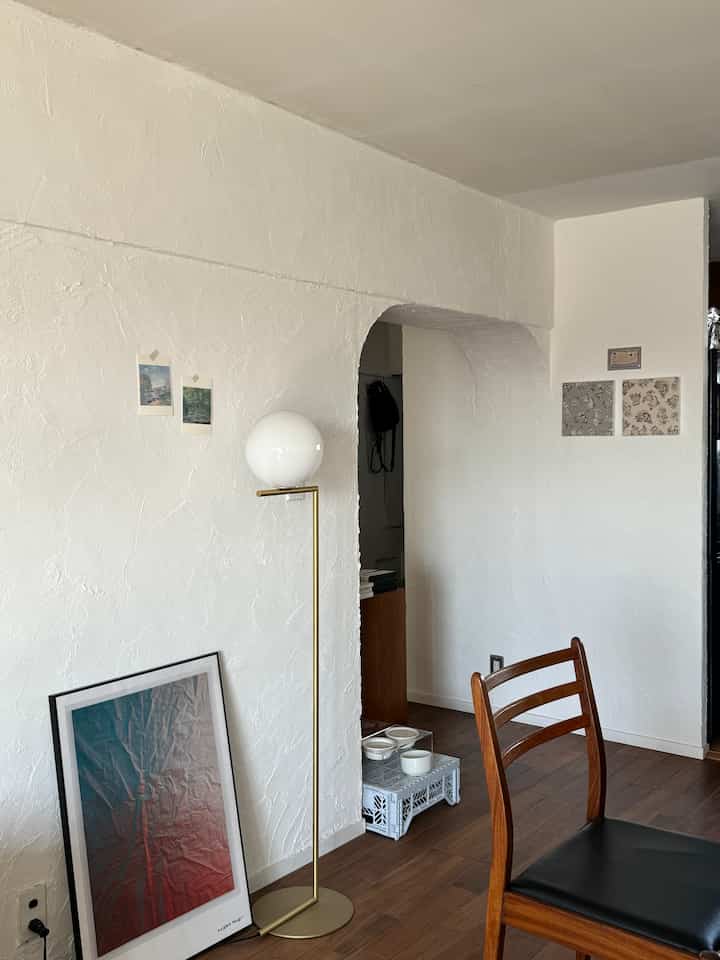 白い壁と木目調の床があるシンプルなダイニング、ゴールドのフロアランプと木製椅子が配置された印象的な空間