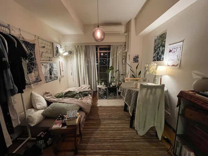 暖かいベージュ色調の狭い寝室、ペンダントライトと植物が配置された落ち着いた雰囲気のインテリア