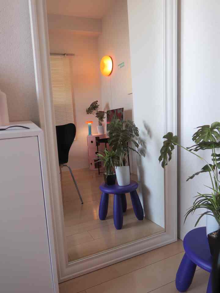 白とモノトーンの廊下、シンプルなインテリアに大きな鏡と紫色のスツールの上の植物が配置された印象的な空間