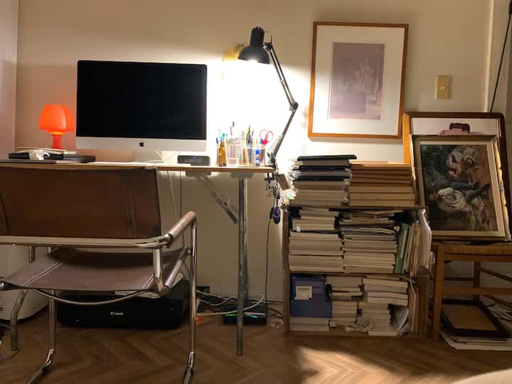 アイボリーの壁と茶色のレザー椅子が配置されたホームオフィス、パソコンと積み上げられた本が散らかった雰囲気を醸し出すインテリア