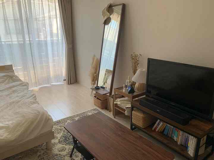 ナチュラルカラーの寝室、木製のベッドと全身鏡、テレビ台が配置された落ち着いた空間