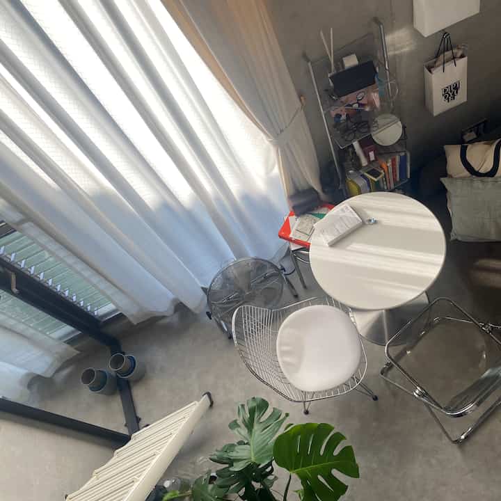 明るい白色と透明感のある素材が特徴のコンパクトなリビング、丸いカフェテーブルとワイヤーチェアが配置された雰囲気のあるインテリア