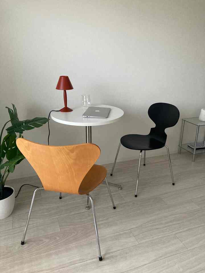 Natural-toned living space featuring a wooden chair, black chair, white round side table with a red lamp, simple and modern design