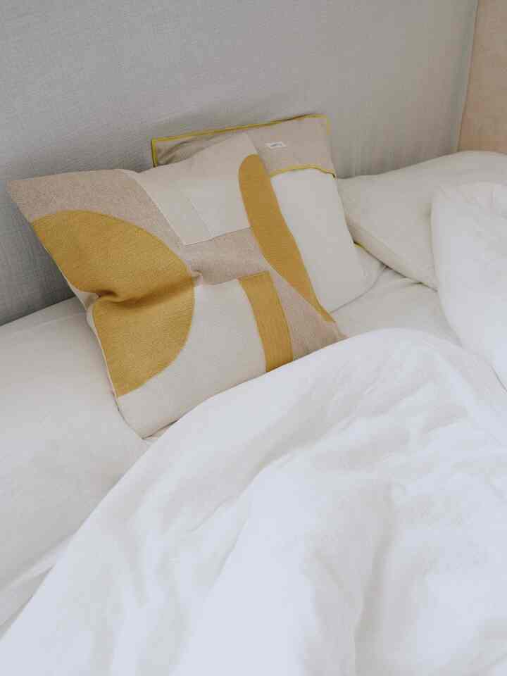 白と黄色のトーンの寝室、黄色のクッションと清潔な白い寝具が配置された雰囲気のある空間