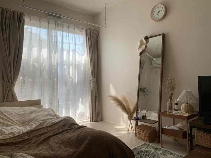 温かみのあるベージュとブラウンのトーンの寝室、カーテンと全身鏡が配置された自然な雰囲気のある空間
