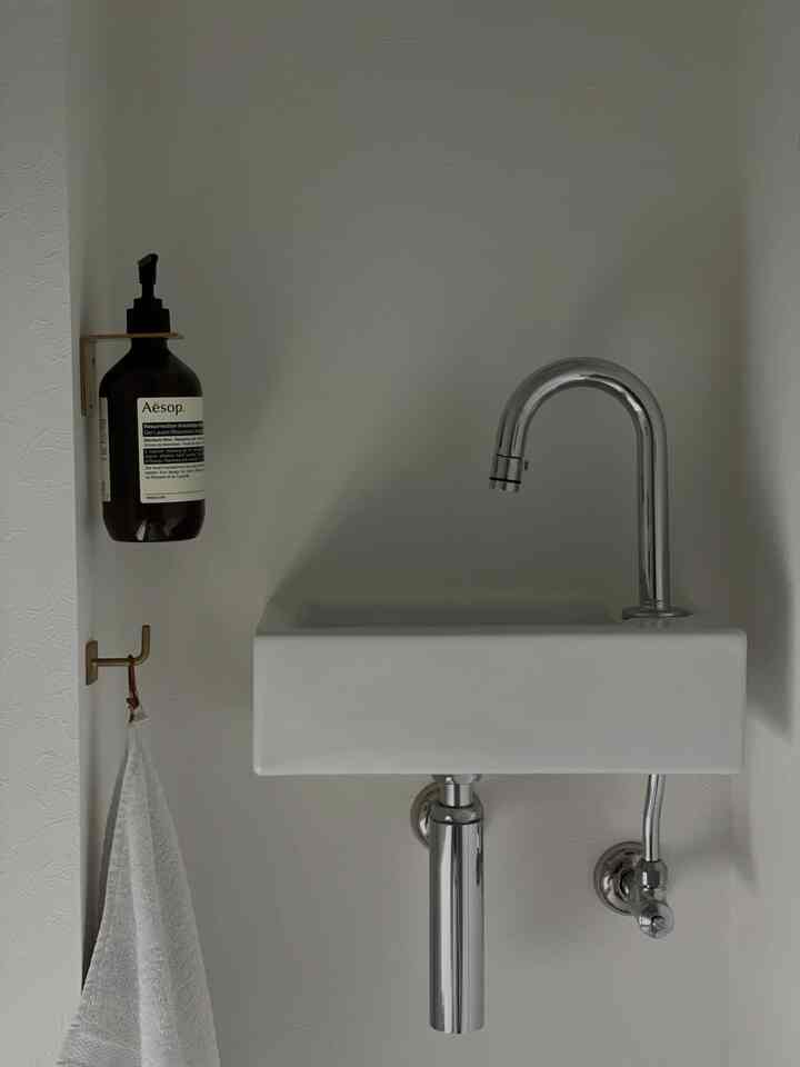 白い壁のコンパクトなバスルームの洗面台、シルバーの水栓と壁掛けディスペンサーが配置された清潔感のあるインテリア