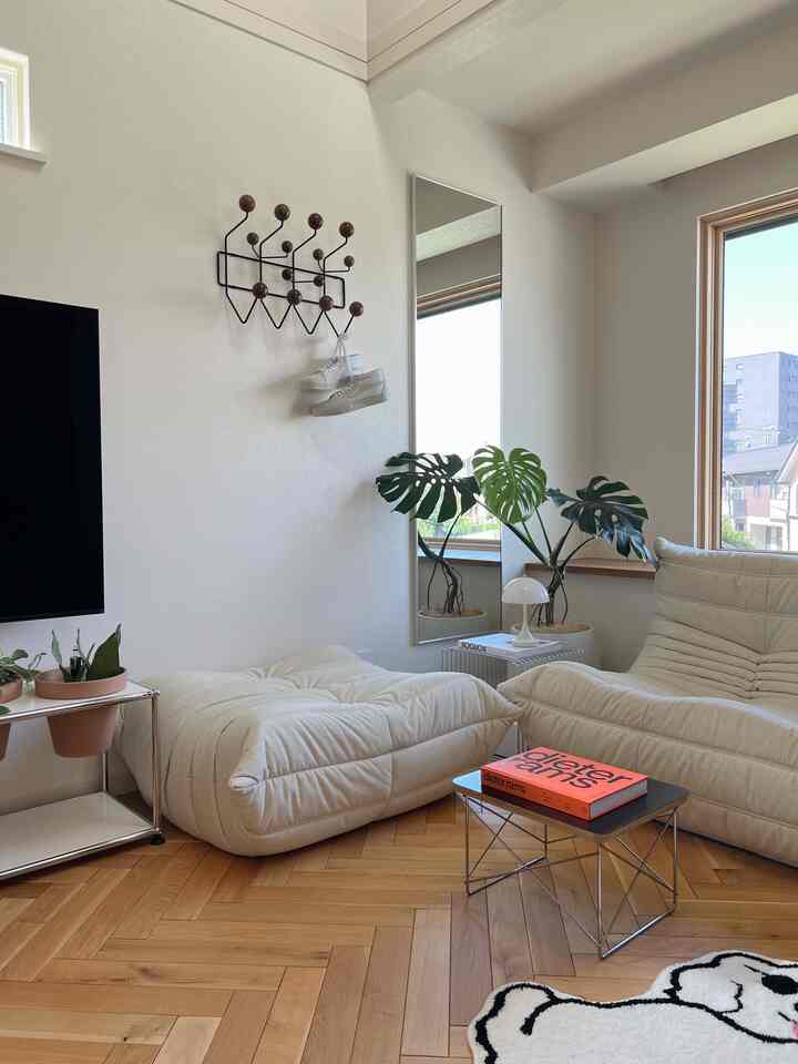 Minimal white and wood-tone living room featuring sofa, ottoman, coffee table, and tall mirror with a calm and cozy atmosphere