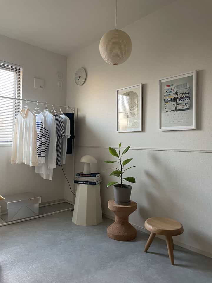 Natural-toned living room featuring wooden and cork stools, plant, white walls, and a round pendant light creating a simple atmosphere