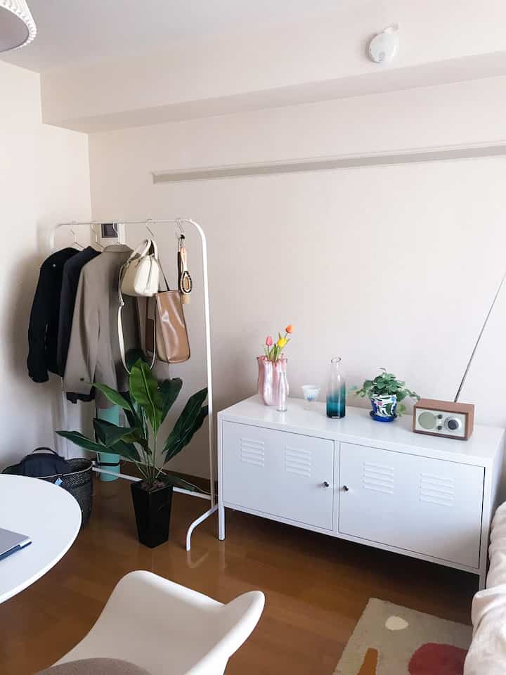 Natural-tone small living space with warm wood flooring, white cabinet, and white clothes hanger rack creating a cozy atmosphere