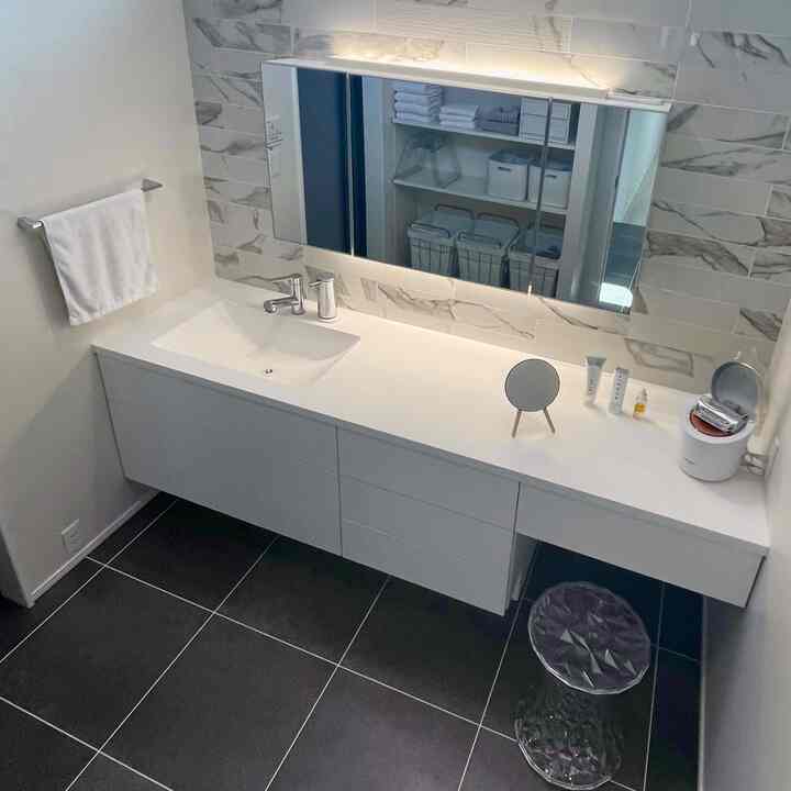 白と黒のトーンのバスルームの化粧台スペース、大型の鏡と透明のスツールが配置された印象的なホテルライクなインテリア