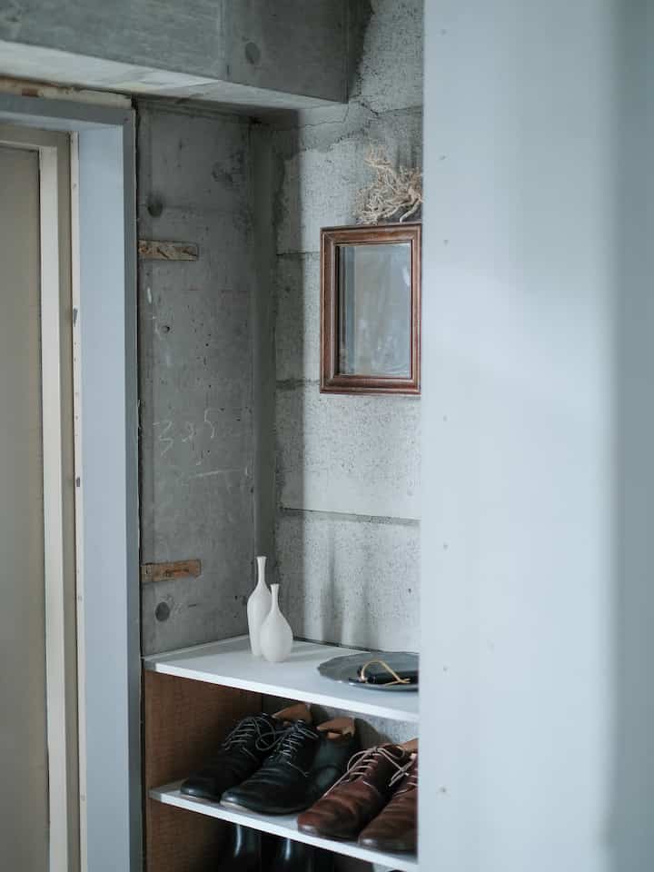 白と茶色のトーンのシンプルな玄関、靴棚と小さな花瓶が置かれた清潔感あるインテリア