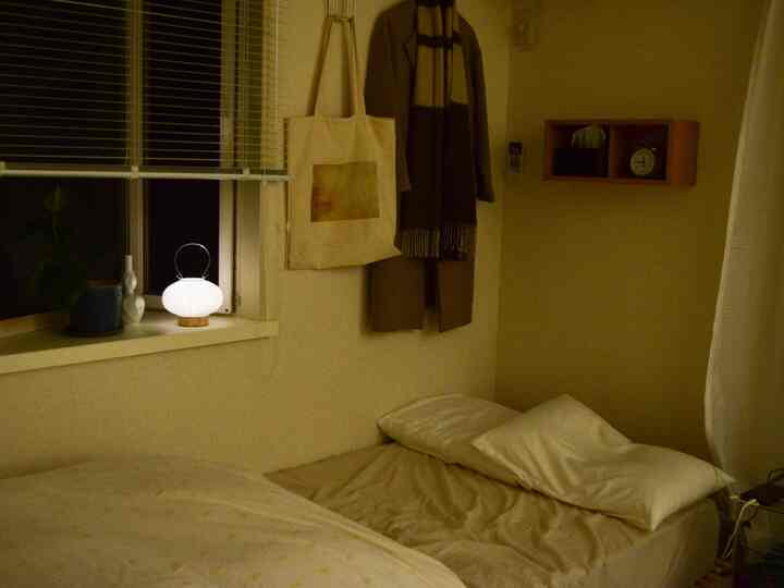 Warm beige and white toned bedroom featuring a bed with pillows, window blinds, and cozy ambient lighting at night