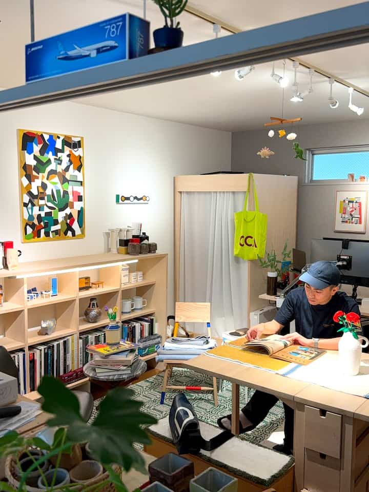 ナチュラルカラーと白を基調としたワンルーム、書棚と机が配置され読書する一人暮らしの空間