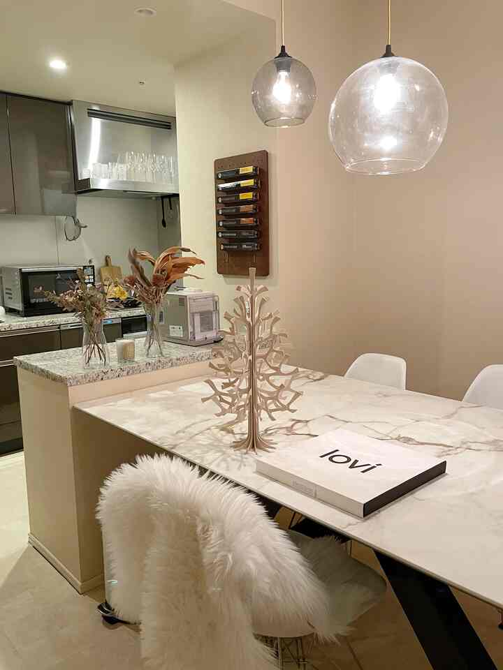 白とナチュラルな色調のキッチンとダイニング、北欧スタイルの木製オブジェとファーの椅子が配置された雰囲気のあるインテリア