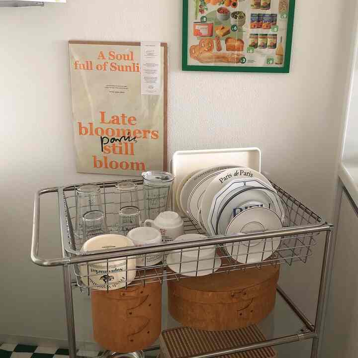 Bright white-walled kitchen featuring a stainless steel dish rack with tableware and wooden boxes, creating a clean natural look