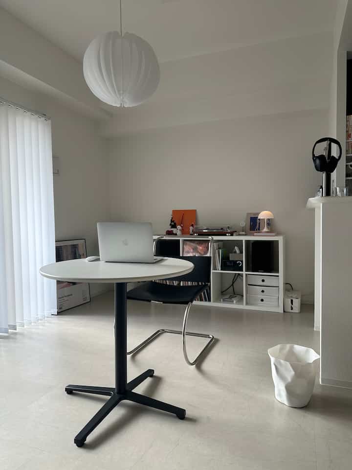 Bright white toned living room featuring a central round table with laptop, clean and modern minimal atmosphere