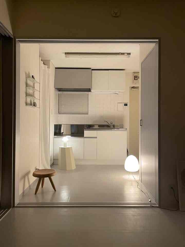 Simple studio apartment kitchen in white and wood tones, featuring stools and indirect lighting creating a warm ambiance