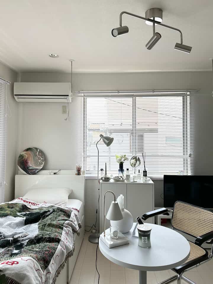 Bright white-toned single bedroom featuring window blinds, floor lamp, and clean interior arrangement