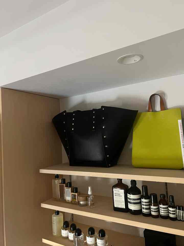白い壁とベージュの木目調棚のある空間、黒とライトグリーンのバッグと整頓された化粧品が配置された雰囲気のあるインテリア