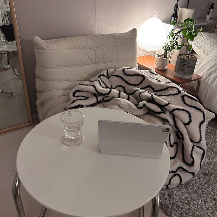 白とアイボリーのトーンが特徴のリビング、快適なソファとパターン入りのブランケットが配置された温かみのある空間