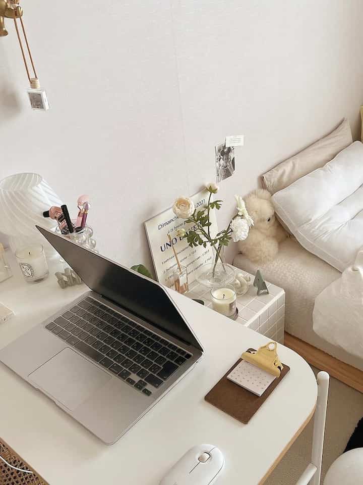 White-tone bedroom and home office featuring a laptop on desk and soft bed setup, creating a simple and cozy atmosphere