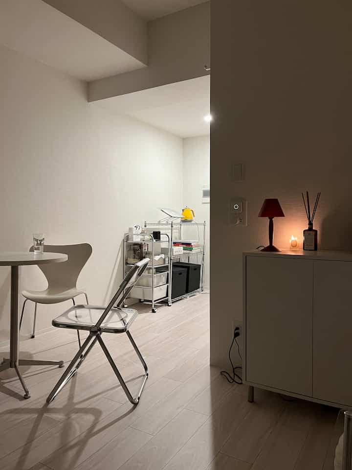 白とグレーのトーンのコンパクトな一人暮らし空間、透明な椅子と金属製収納ラックが配置されたミニマルな雰囲気の部屋