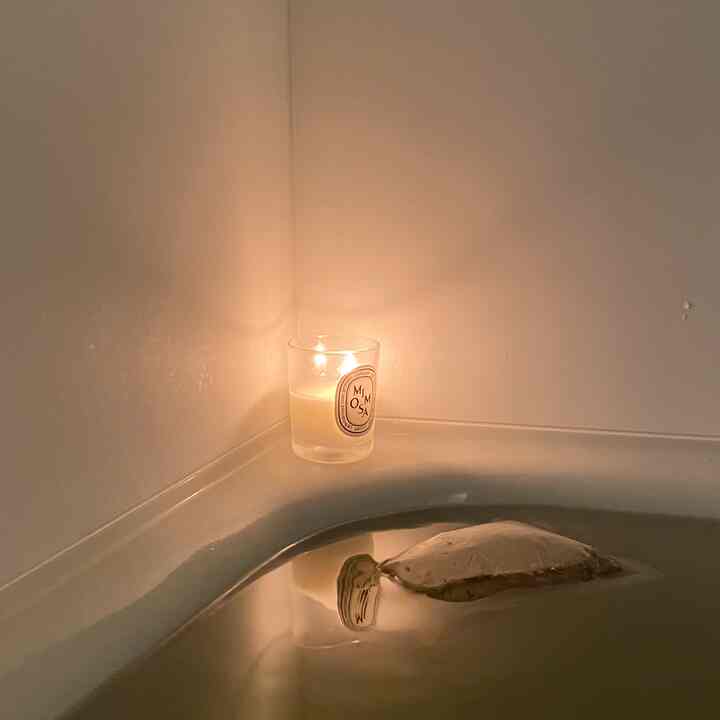 White bathroom corner featuring a lit candle with warm light on the bathtub edge, creating a quiet and serene atmosphere
