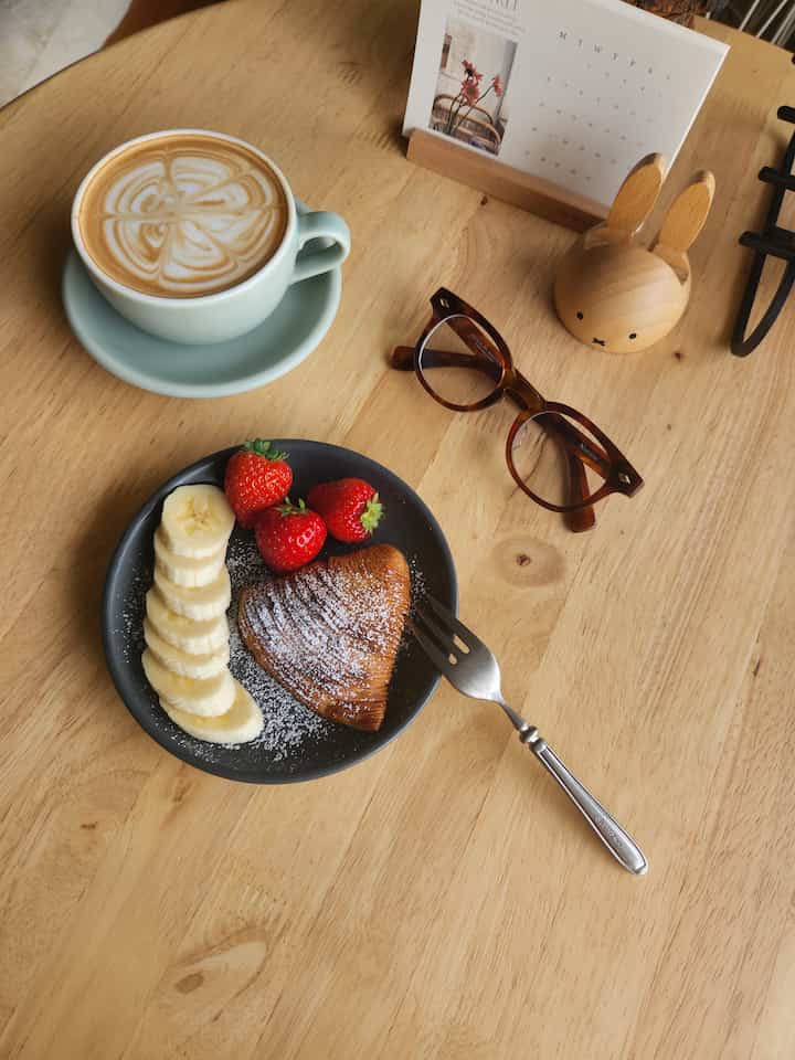 明るい木目調のダイニングテーブル上におうちカフェのセット、皿とマグカップ、木製のウサギ型スマホスタンドが配置された落ち着いた雰囲気のインテリア