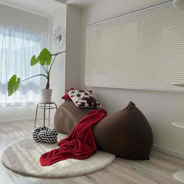 Soft white, brown, and red toned living room featuring a bean bag sofa with cushions and throw blanket, creating a cozy atmosphere