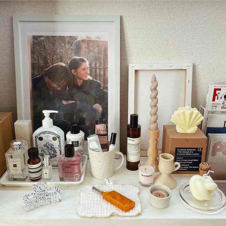Bright white-toned corner storage space featuring various candles, a speckled mug, perfumes, and decorative objects in a cozy arrangement