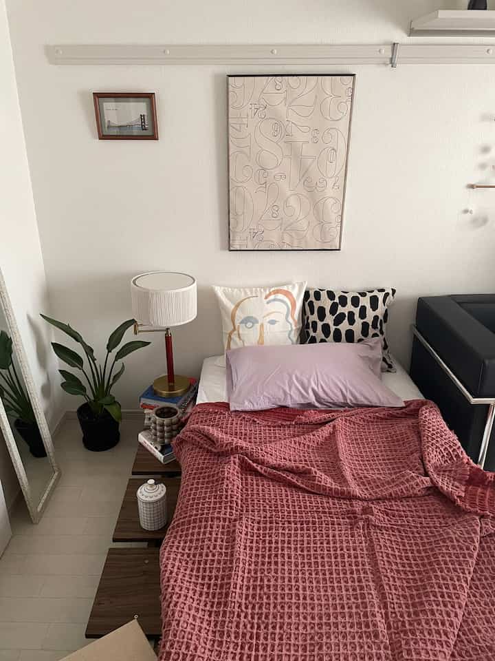 Modern bedroom with white walls featuring a bed dressed in red waffle-pattern blanket and decorative cushions for a cozy atmosphere