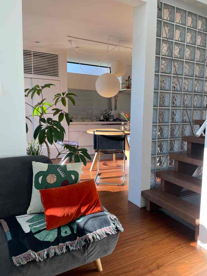 Warm wooden flooring and sunlight-filled living room featuring sofa and cushions, creating a cozy atmosphere