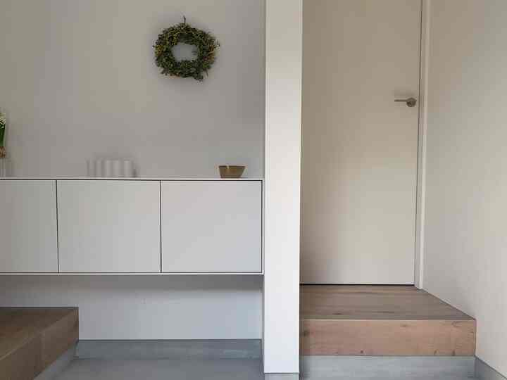 A simple entrance space with white and wood tones, featuring a white shoe cabinet and natural wreath for a clean look