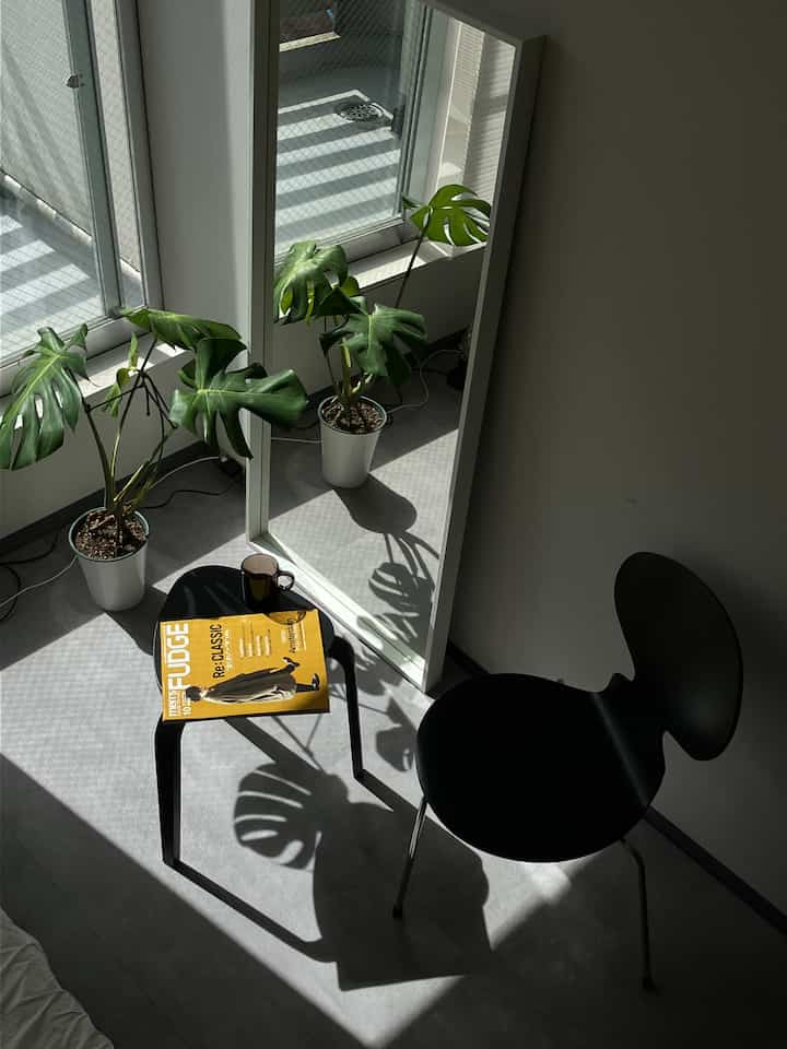 Bright modern Nordic space with white walls and floor, black stool and chair arranged for reading by natural light