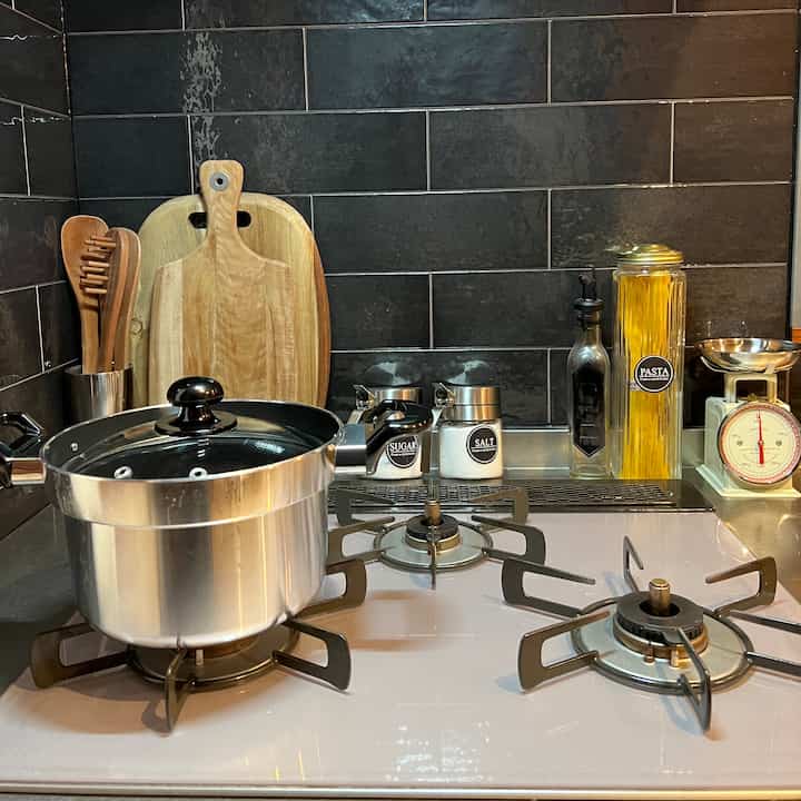 黒いタイルの壁面と木目調の調理器具が配置された白いガスコンロのキッチン、落ち着いた雰囲気のあるインテリア